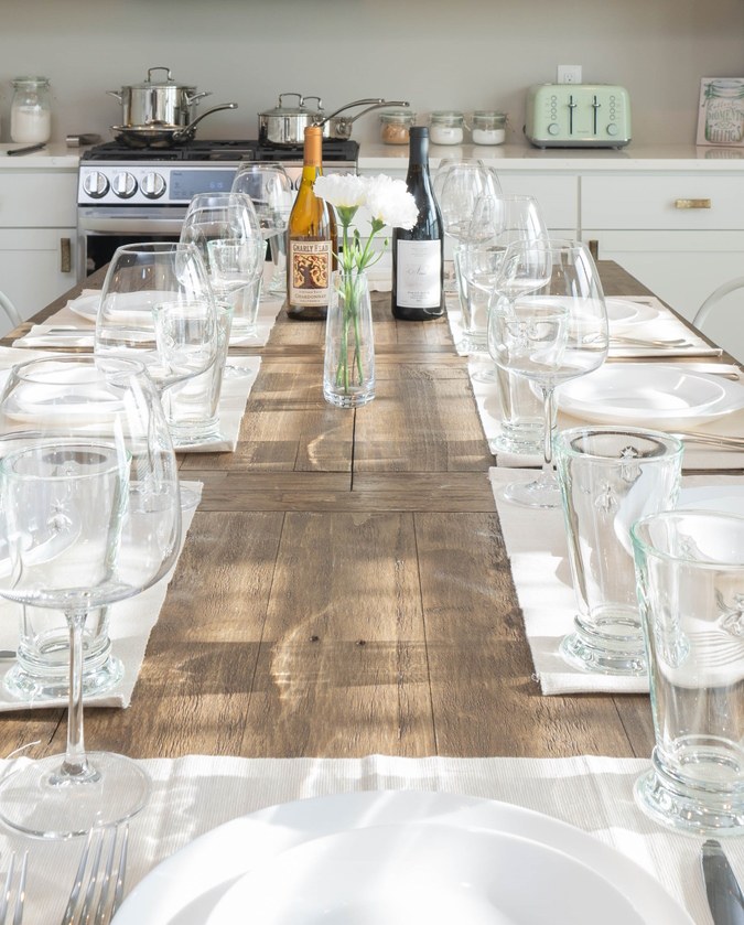 Long dining table set with wine glasses, with the kitchen behind
